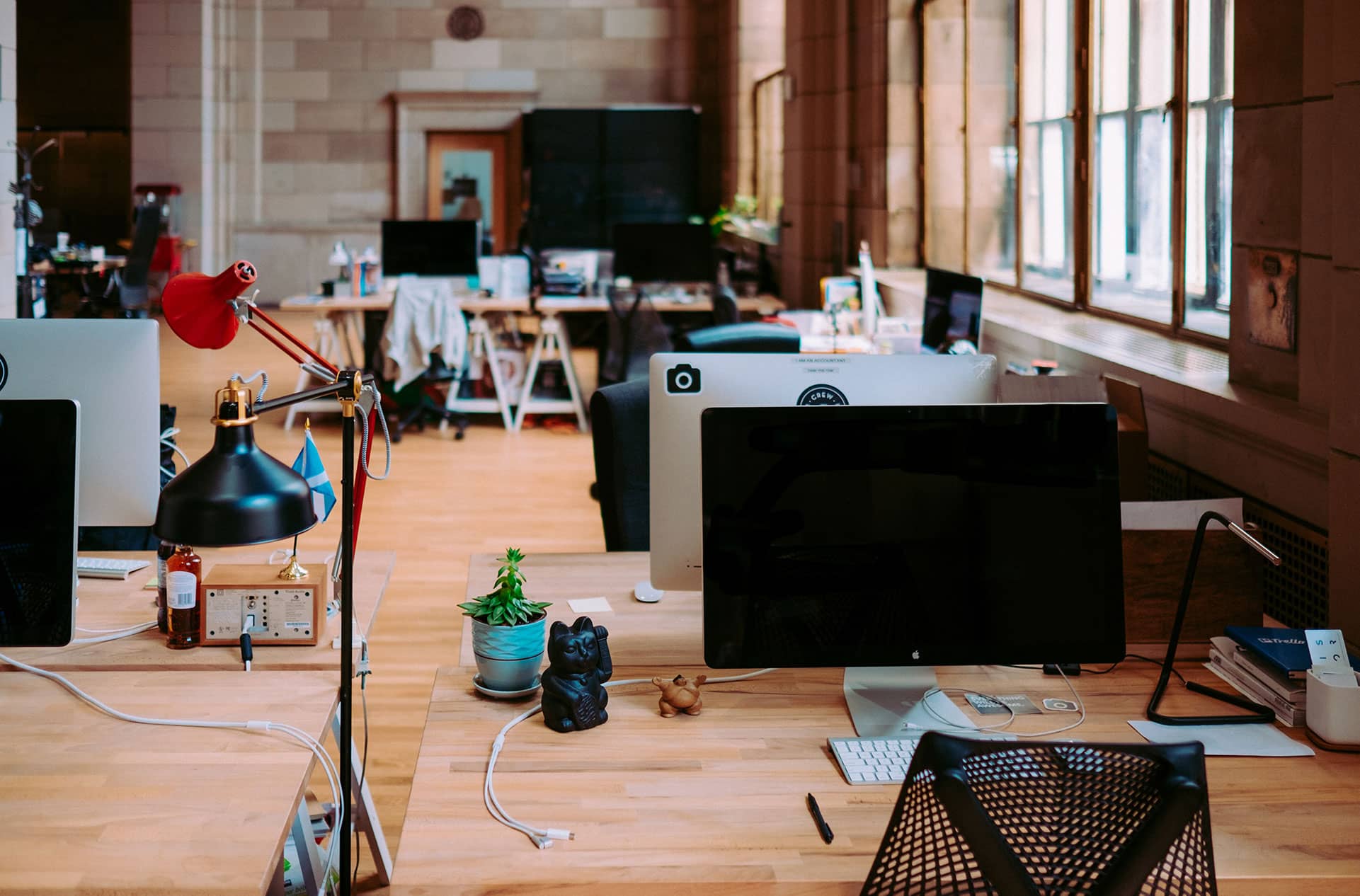 Modern open office workspace with desktop computers, wooden desks, and natural light from large windows