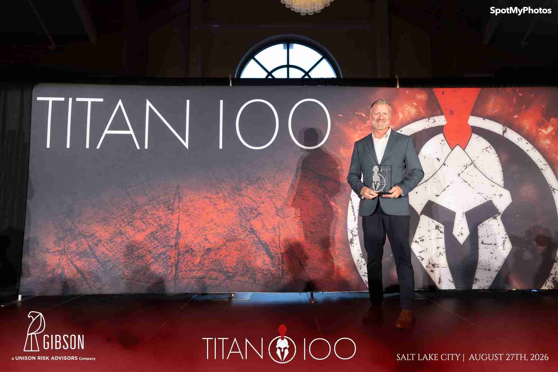 Greg Weeks holding his Titan 100 award on stage at the 2026 Titan 100 event in Salt Lake City.